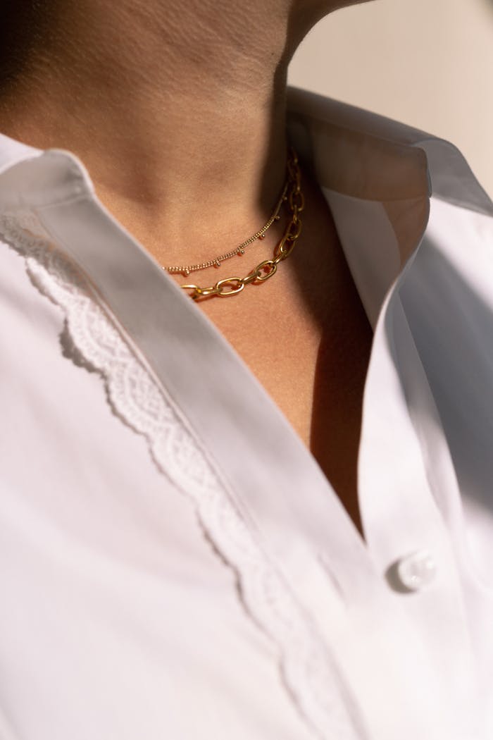 ours-journey Elegant fashion image showcasing two gold necklaces layered over a crisp white shirt.